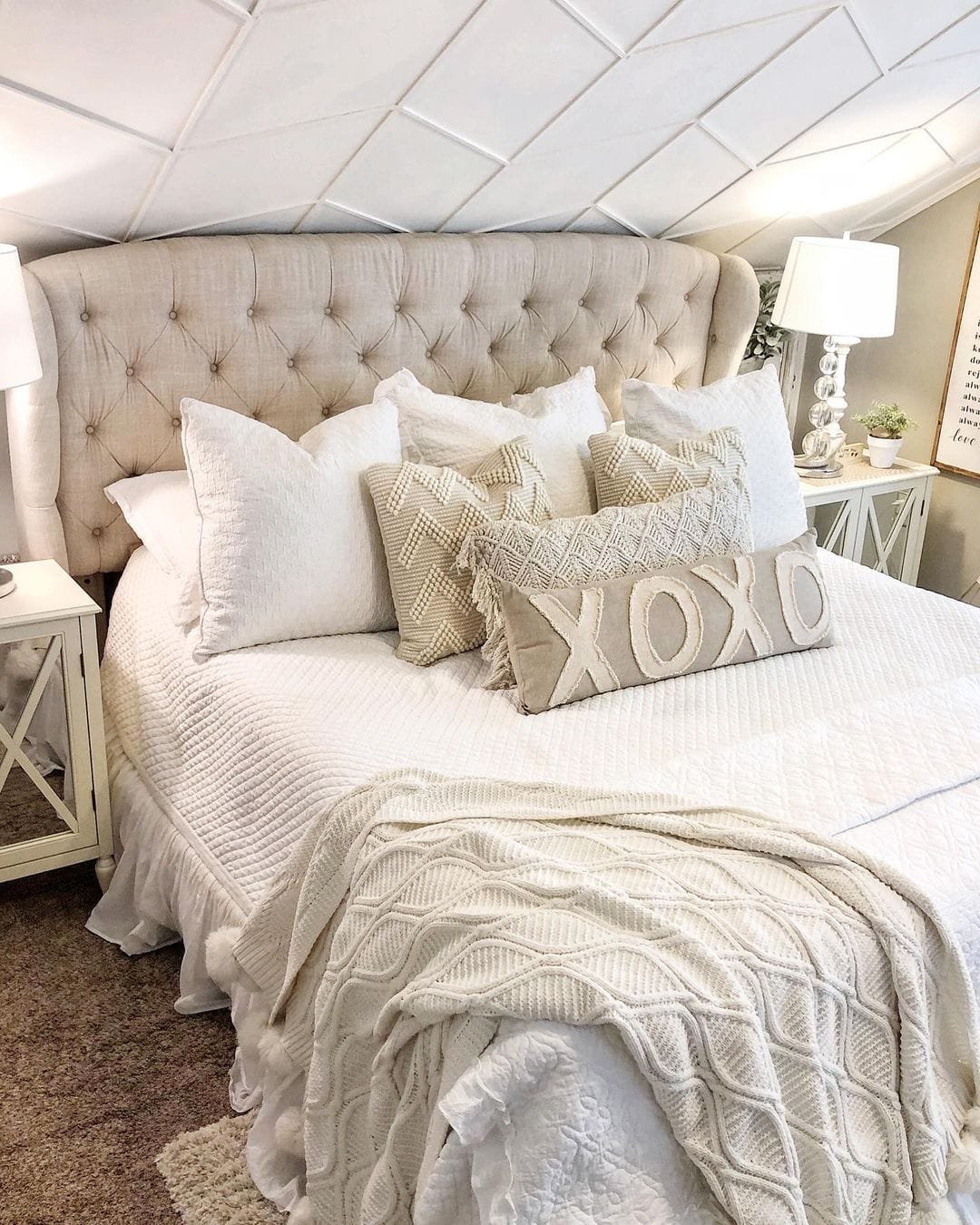 Elegant bedroom featuring a large tufted headboard, Modern Farmhouse bedding, decorative pillows with "XOXO," and two bedside lamps.