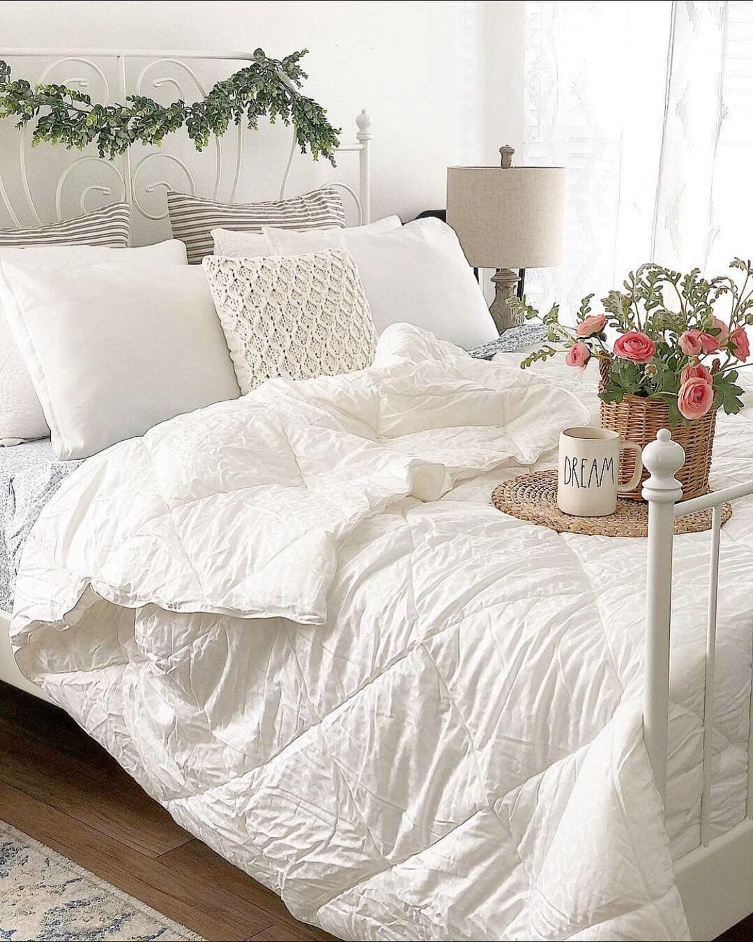 A cozy bedroom with a white modern farmhouse quilted bed, floral accents on a side table, and subtle greenery above the headboard.