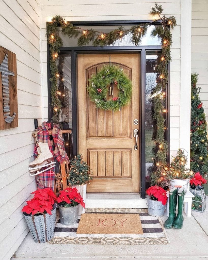 Christmas front porch decor with string lights around a wooden door with sidelights and floor vignettes using Christmas-inspired items.