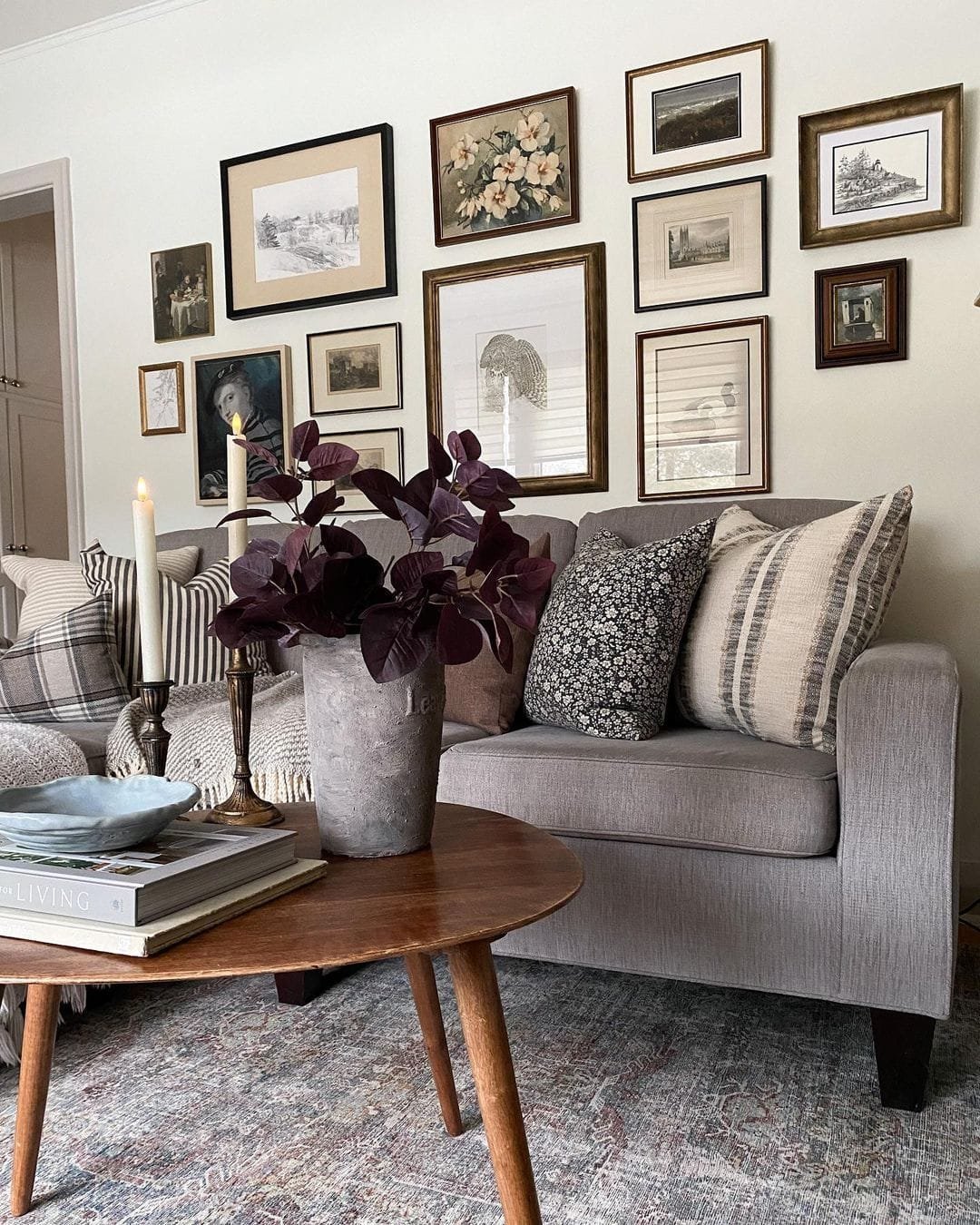 Cozy living room corner featuring a gray sofa, wooden coffee table, and a wall decorated with an assortment of vintage framed artworks.