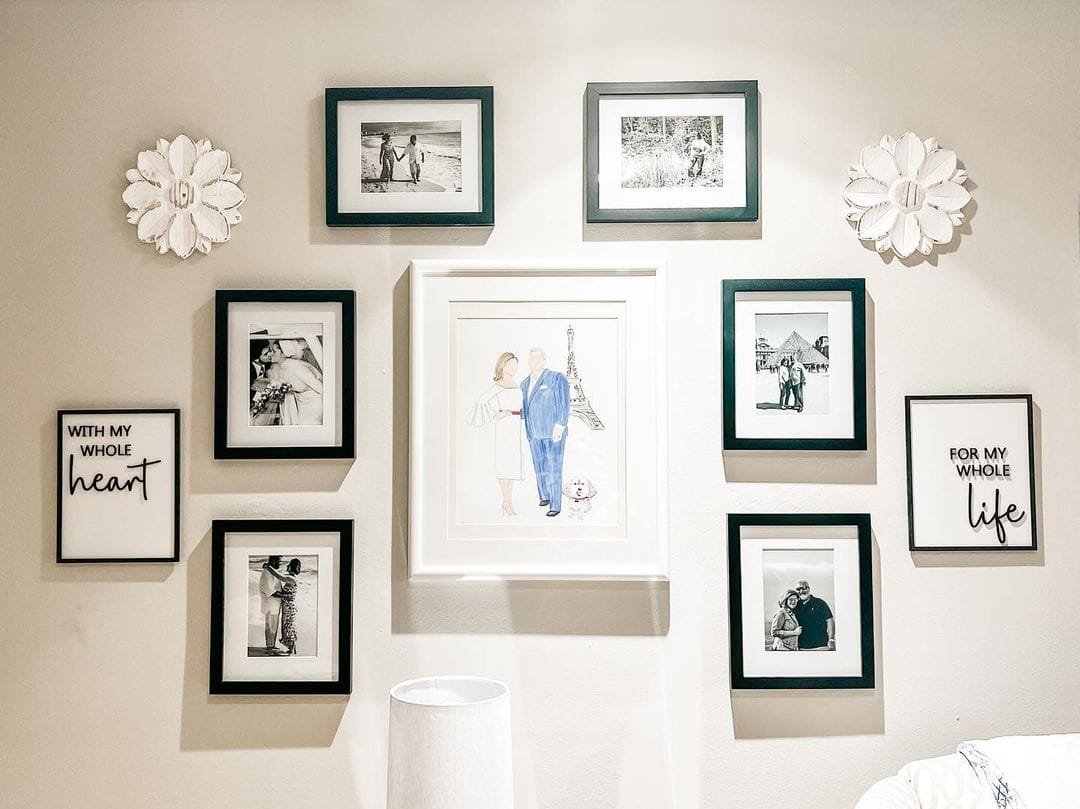 A wall adorned with various framed photos and artworks, including a central colorful illustration of a woman with a child, surrounded by vintage frames and floral decorations.