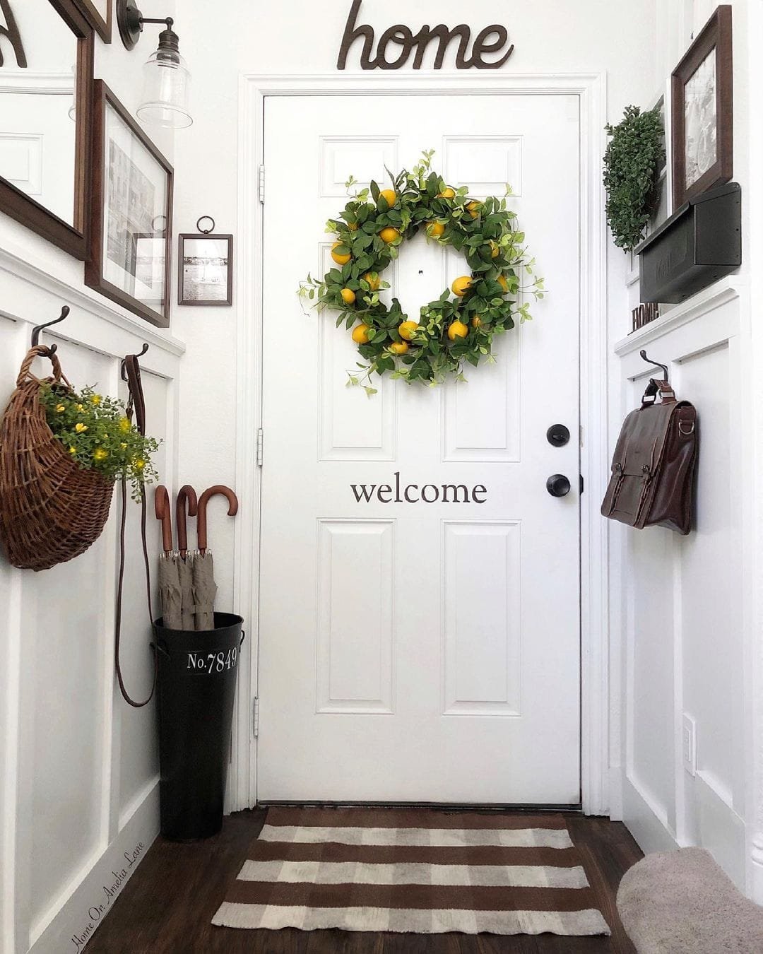 A white front door adorned with a yellow and green floral wreath, capturing the essence of summer colors, and a "welcome" mat, flanked by wall-mounted decor and accessories.