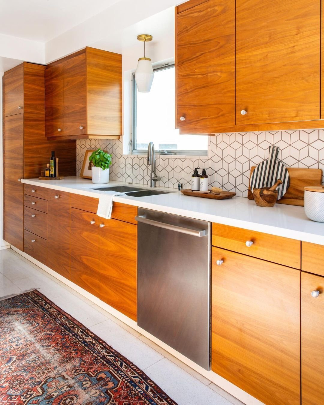 Modern kitchen interior with wooden cabinets, stainless steel appliances, a Mid-Century geometric backsplash, and a patterned rug.