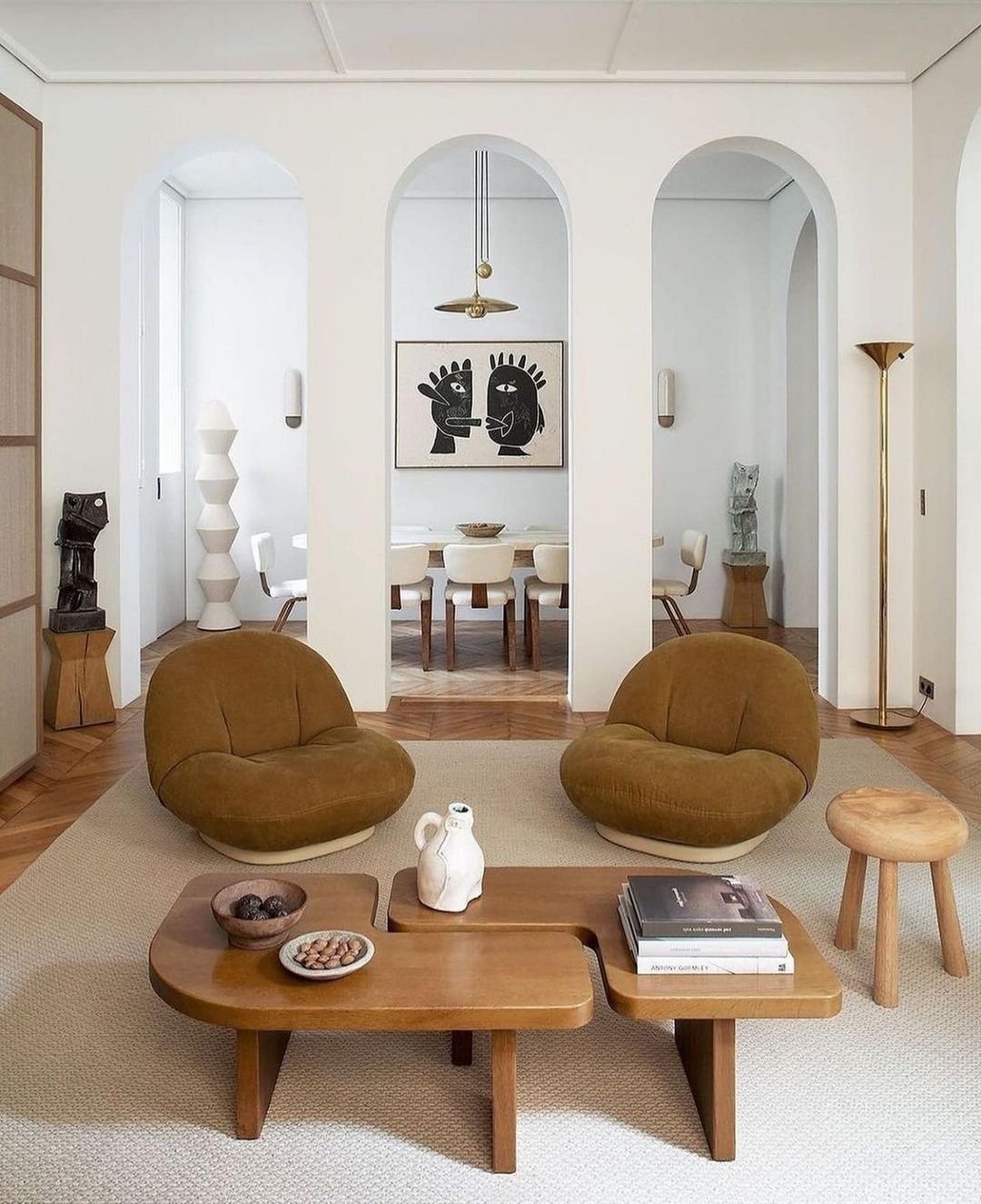 A modern living room with two brown lounge chairs, a wooden coffee table adorned with decorative items, and a view into a dining area showcasing a large black-and-white artwork on the wall—truly exemplifying Minimalist Living: How Japandi Decor Can Help Simplify Your Life.