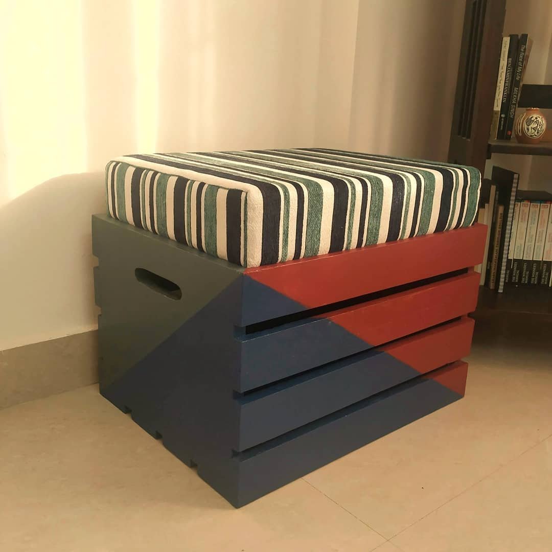 A rustic wooden crate, painted blue and red with a striped cushion on top, serves as a makeshift ottoman. This is just one of the 10 Wooden Crates Decor Hacks to Add Rustic Charm to Your Home.