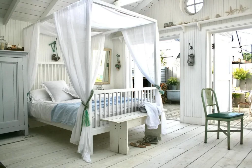 light airy fabrics, neutral white walls and floor color scheme, natural wood furniture, and sea-inspired accents make this bedroom a beach decorated bedroom sanctuary to unwind in.