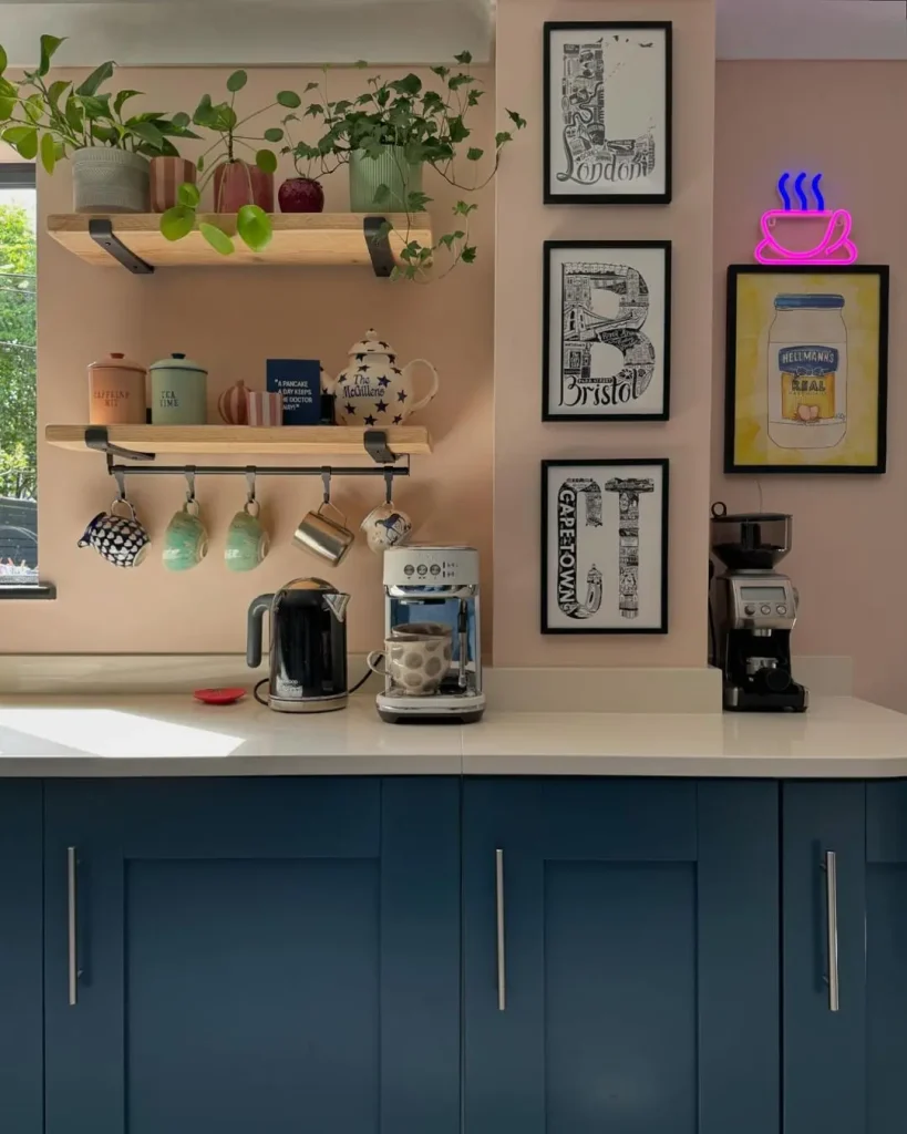 A kitchen corner featuring blue cabinets, a coffee machine, a kettle, mugs on hooks, shelves with plants and jars, framed artwork on the wall—perfect inspiration for how to create a stunning gallery wall for every room—and a neon coffee cup sign.