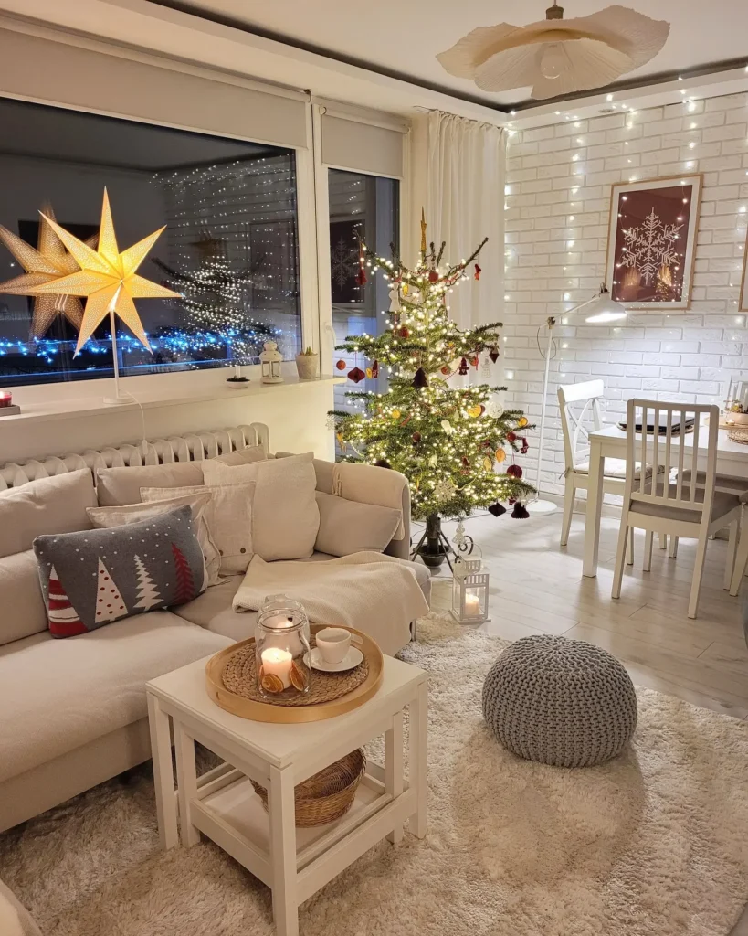 A cozy living room decorated for Christmas with a lit tree, star lantern, string lights, candles, and neutral-colored furniture showcases the perfect christmas decoration for small living room spaces next to a festive dining area wall display.