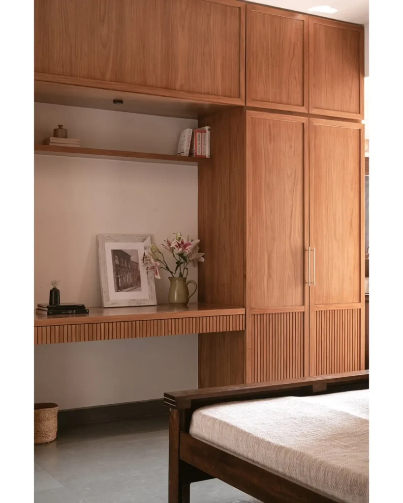 Minimalist bedroom with built-in wooden wardrobe, overhead cabinets, and integrated desk with open shelving.
