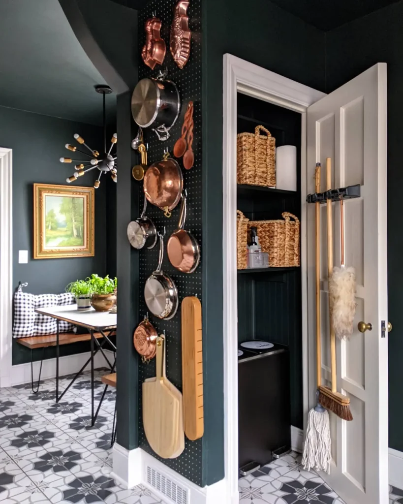 Moody green kitchen featuring a wall pegboard with hanging copper pots and utensils, woven basket storage, and black-and-white patterned tile floor.